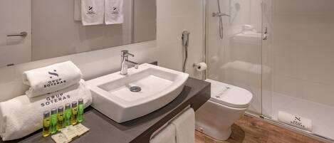 A modern bathroom with a sink, toilet, and glass-enclosed shower. There are towels and toiletries on the counter.