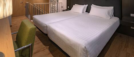 A large bed with white linens, a green upholstered chair, and a wooden floor.