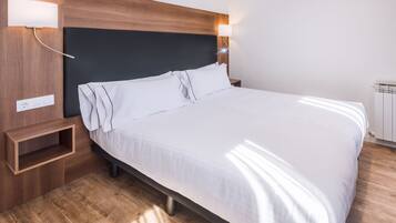 Una cama bien hecha con sábanas blancas, cabecera de madera y lámparas de noche.