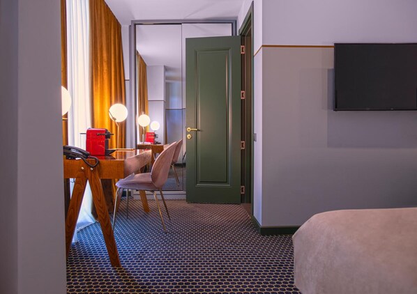 A hotel room with a bed, a desk with a chair, a television, and a door leading to another room. - Hotel Zemeli (Tbilisi)