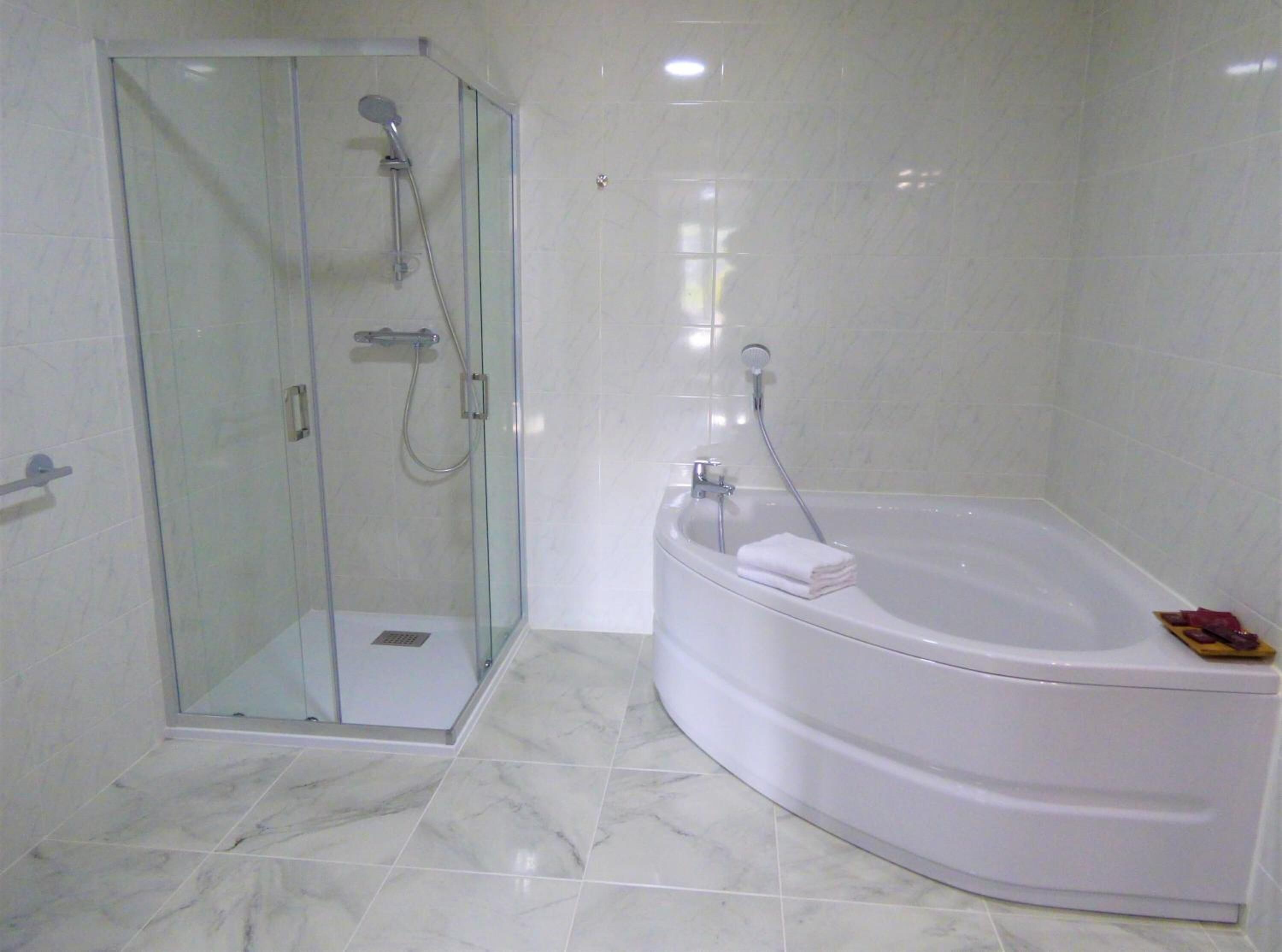 Un baño con ducha envuelta en vidrio, una bañera blanca y piso de mármol.