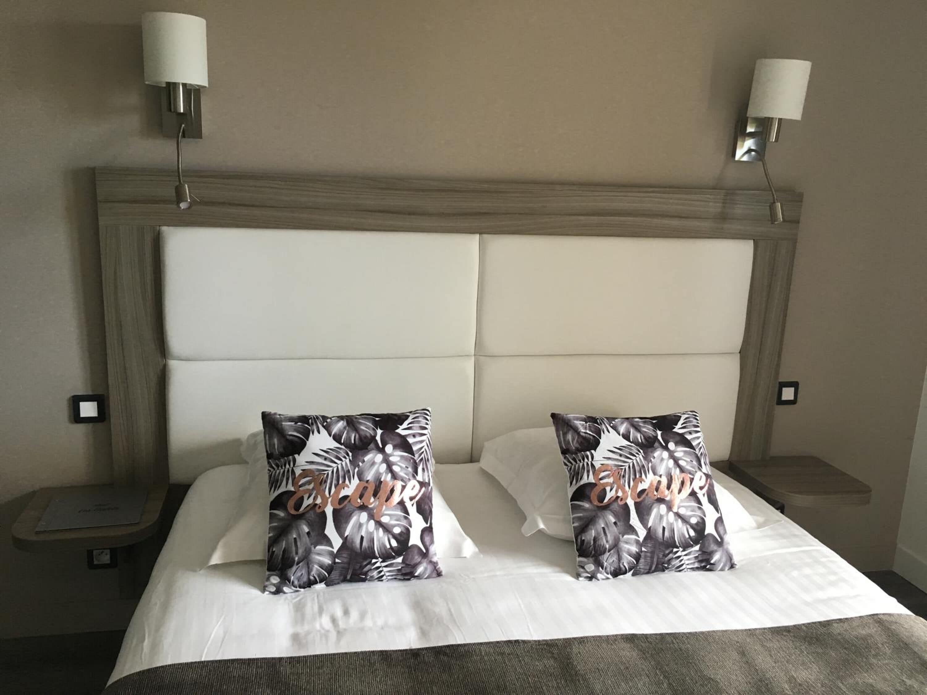 A hotel room with a large bed, two nightstands, and wall-mounted lamps.