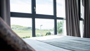 A room with a large window, a bed, and a view of a green landscape. - Hôtel Les Galets (Criel-sur-Mer)