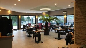 A modern restaurant with indoor seating, large windows, and a central potted plant. - Hôtel Les Galets (Criel-sur-Mer)