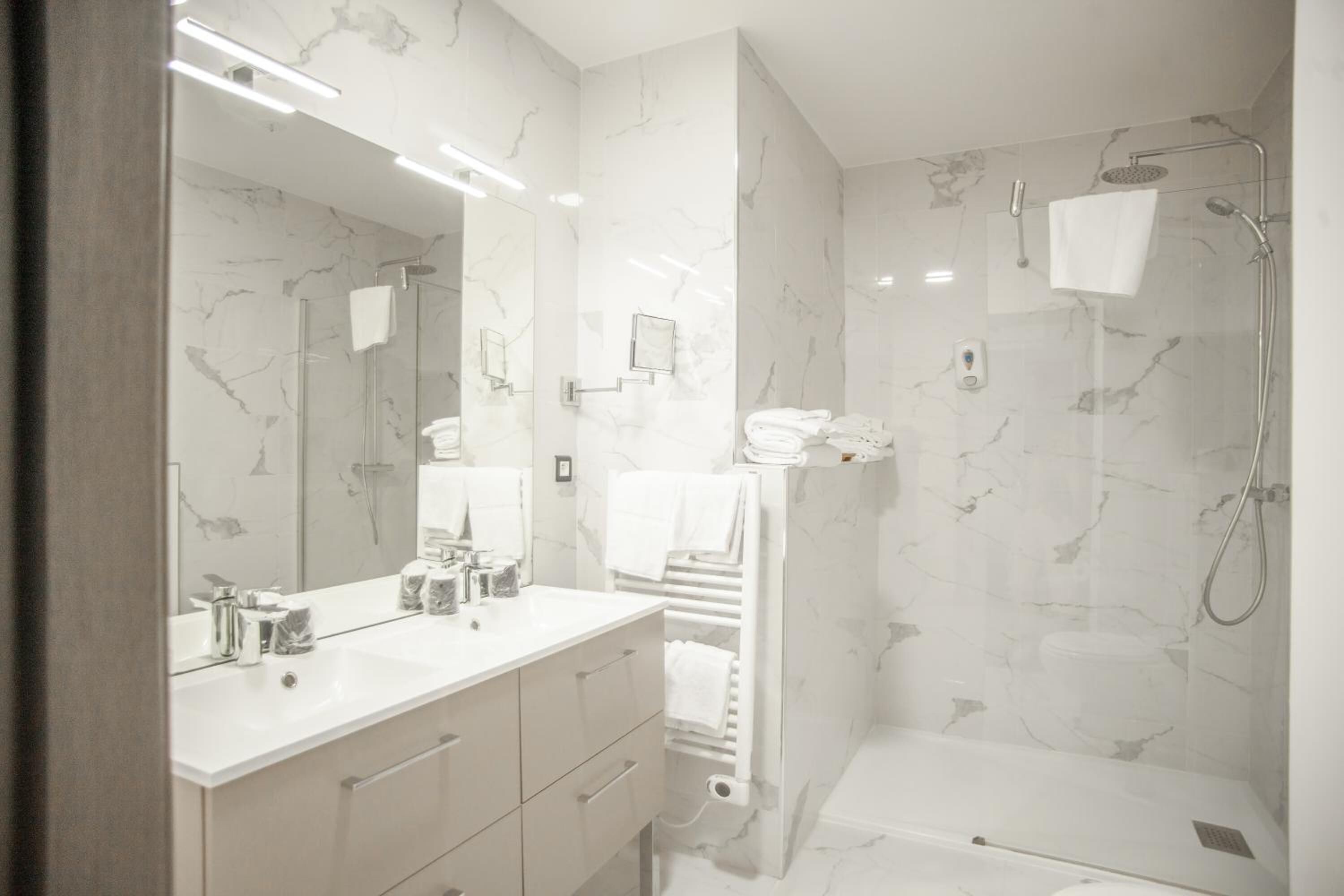 A modern bathroom with marble walls, a dual sink vanity, a glass shower enclosure, and a towel rack.