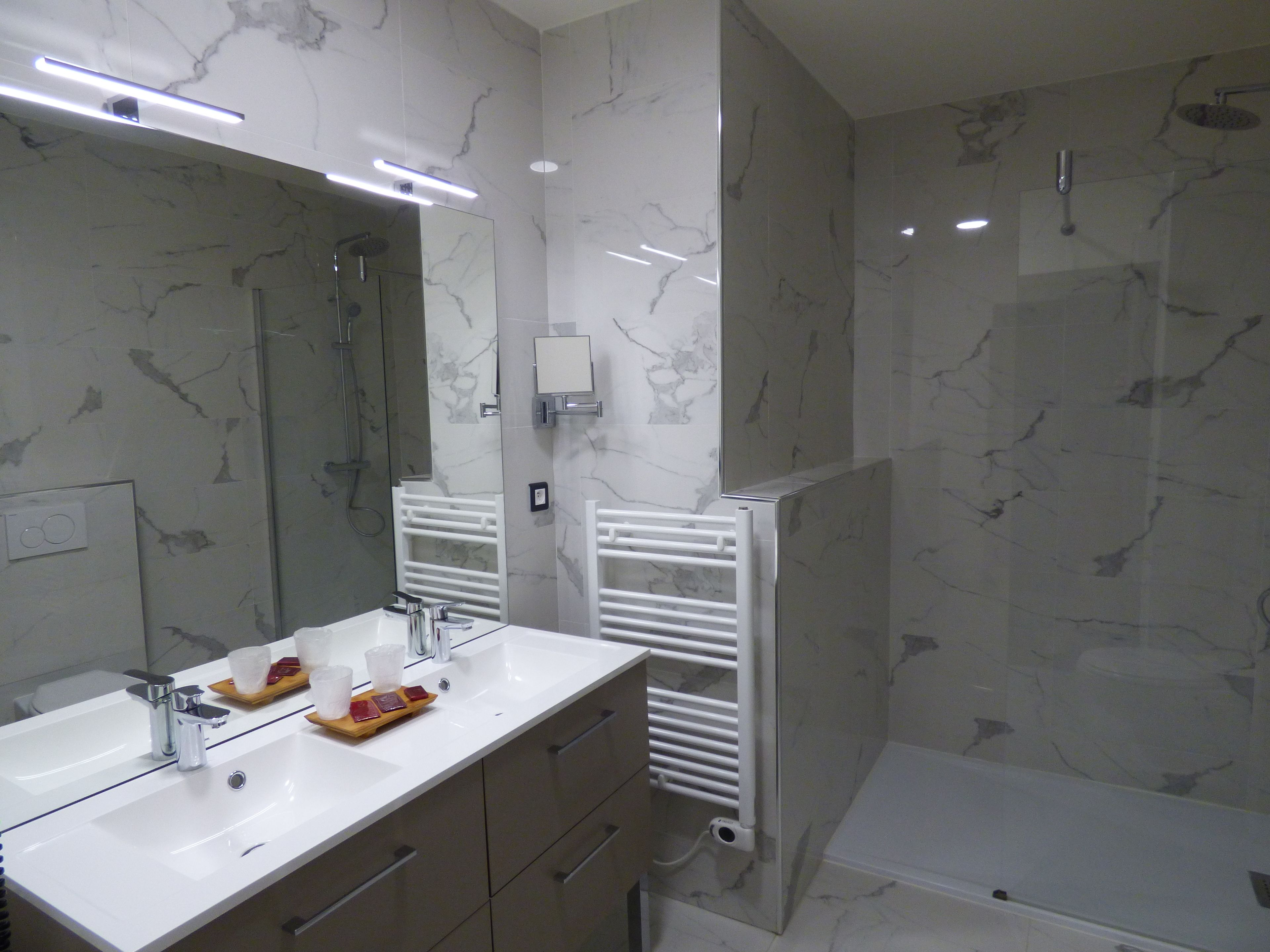 A modern bathroom with a large mirror, two sinks, a shower, and a bathtub.