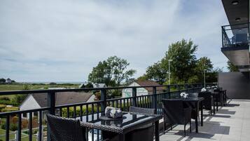 Una terraza con mesas al aire libre, vistas del paisaje y una edificación al fondo.