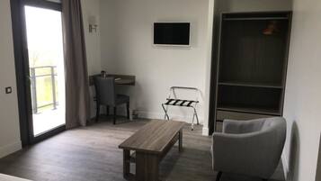 Una habitación de hotel moderna con suelo de madera, una cama, un sillón gris, un escritorio con silla, un televisor montado en la pared y un armario con espacio para colgar ropa.