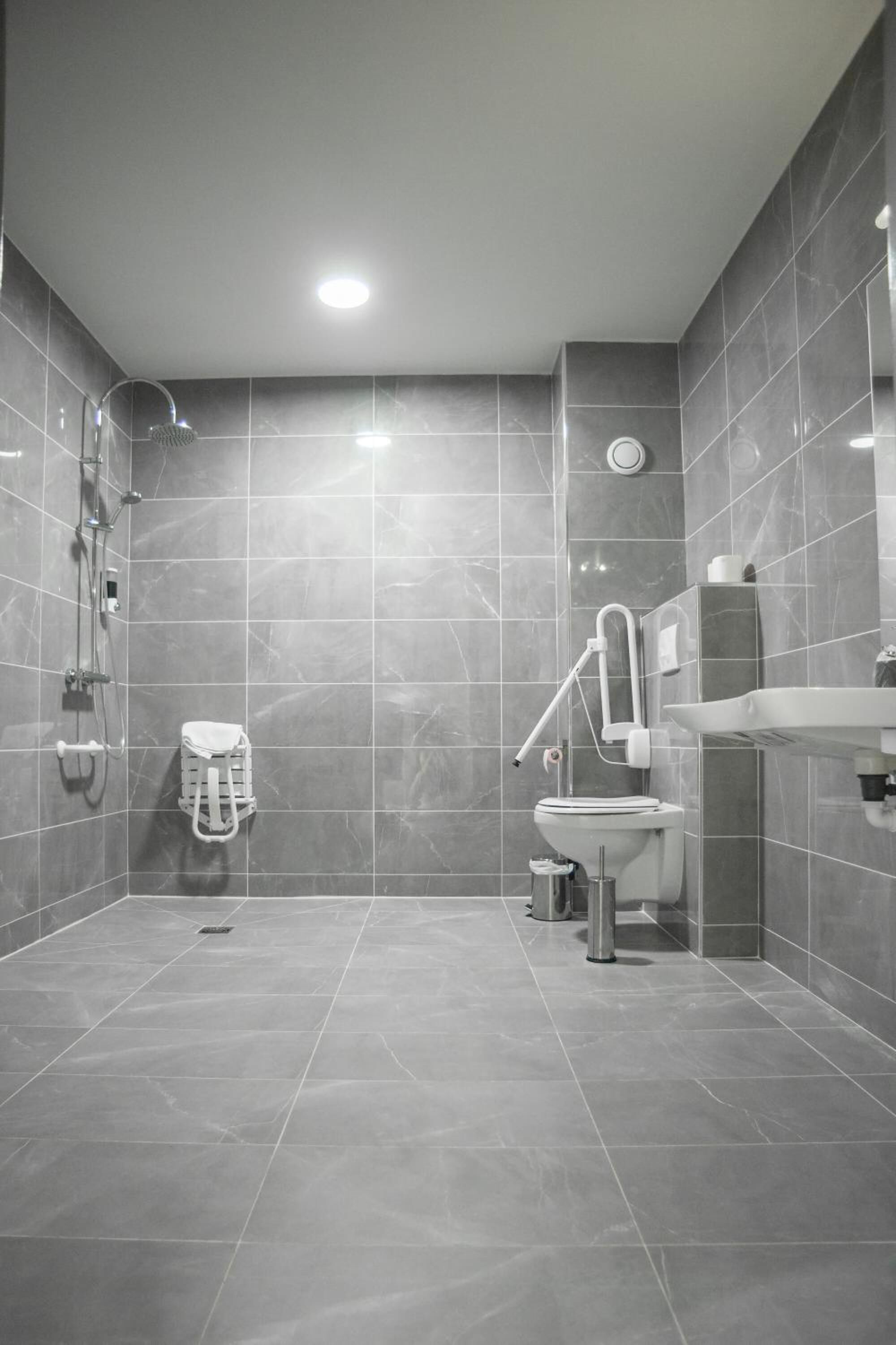 Een moderne badkamer met grijze tegels, een douche, toilet en wastafel.