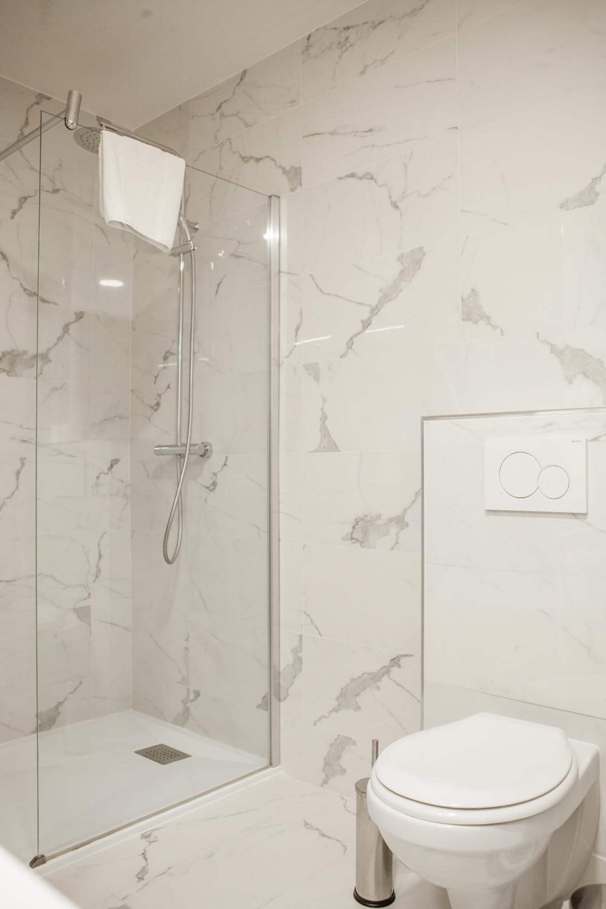 Et badeværelse med en glasafskærmet bruseniche, toilet og vægge med marmorlook.