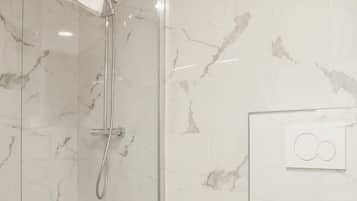 Et badeværelse med en glasafskærmet bruseniche, toilet og vægge med marmorlook.