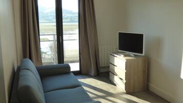 Een moderne woonkamer met een grijze bank, een flatscreen televisie op een houten dressoir, en een uitzicht op een verafgelegen landschap door een schuifdeur van glas.
