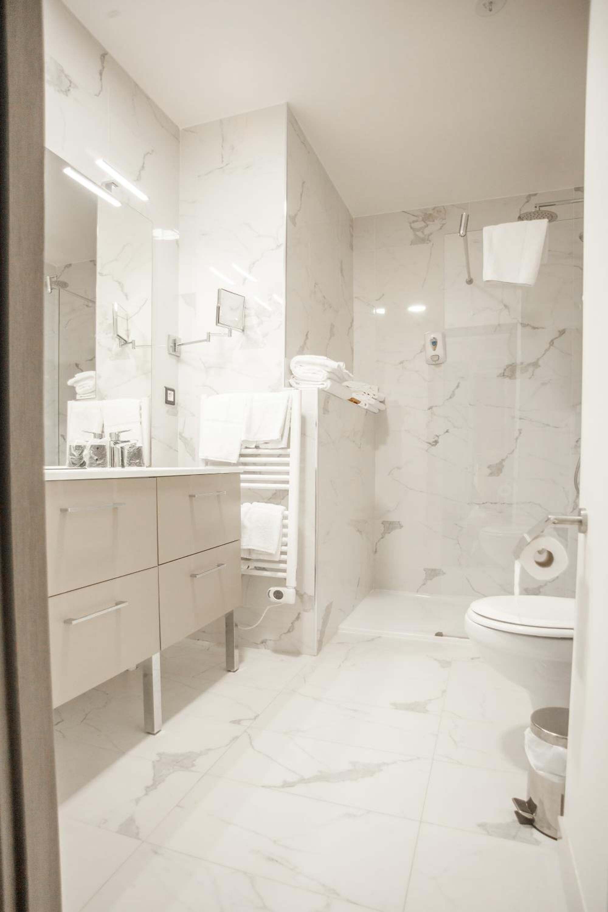 A modern bathroom with marble tiles, a large mirror, a toilet, and a shower area.