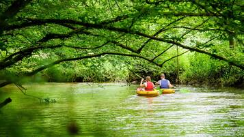 Two people kayaking on a river surrounded by dense green foliage.