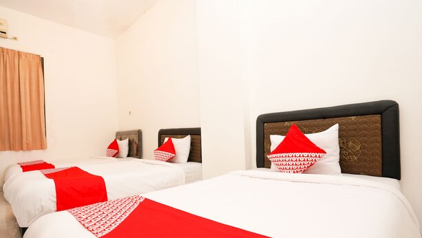Quarto de hotel com duas camas, cada uma com roupa de cama branca e detalhes em vermelho, e uma cabeceira marrom.