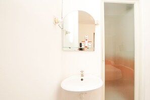 A bathroom with a white sink, a mirror, and a door leading to a room.