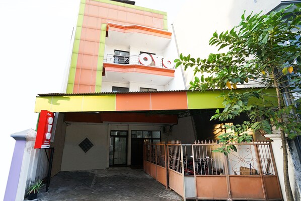 A multi-story building with a green and orange facade, a gated entrance, and a small tree in front.