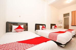 A hotel room with three beds, each with white bedding and red accents.