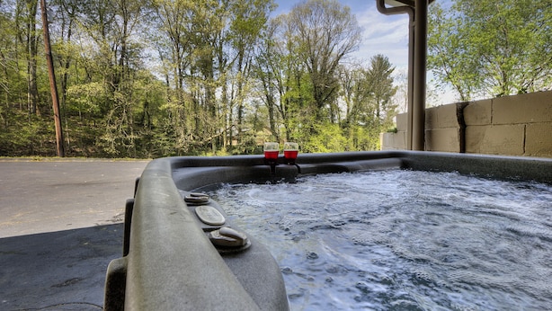 A hot tub with a stone edge, surrounded by a concrete wall and trees. - Blessed Mountain Acres w/ Leather Recliners, Hot tub, Swing close to parkway (Sevierville)