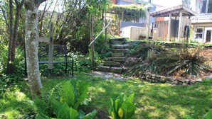Un jardín con un banco de madera, escalones de piedra y abundante vegetación.