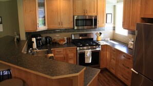 Una cocina con armarios de madera, un microondas de acero inoxidable, una estufa a gas y un refrigerador.