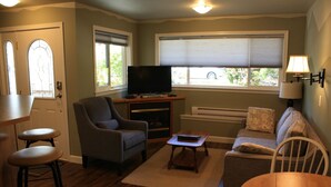 Una sala de estar con televisor, un sofá, un sillón, una mesita y una zona de bar con taburetes.