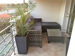 A balcony with wicker furniture, a potted plant, and a view of the road. - Sunny Estate (Nin)