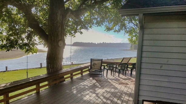 Een houten terras met een schommel, stoelen en uitzicht op een meer.