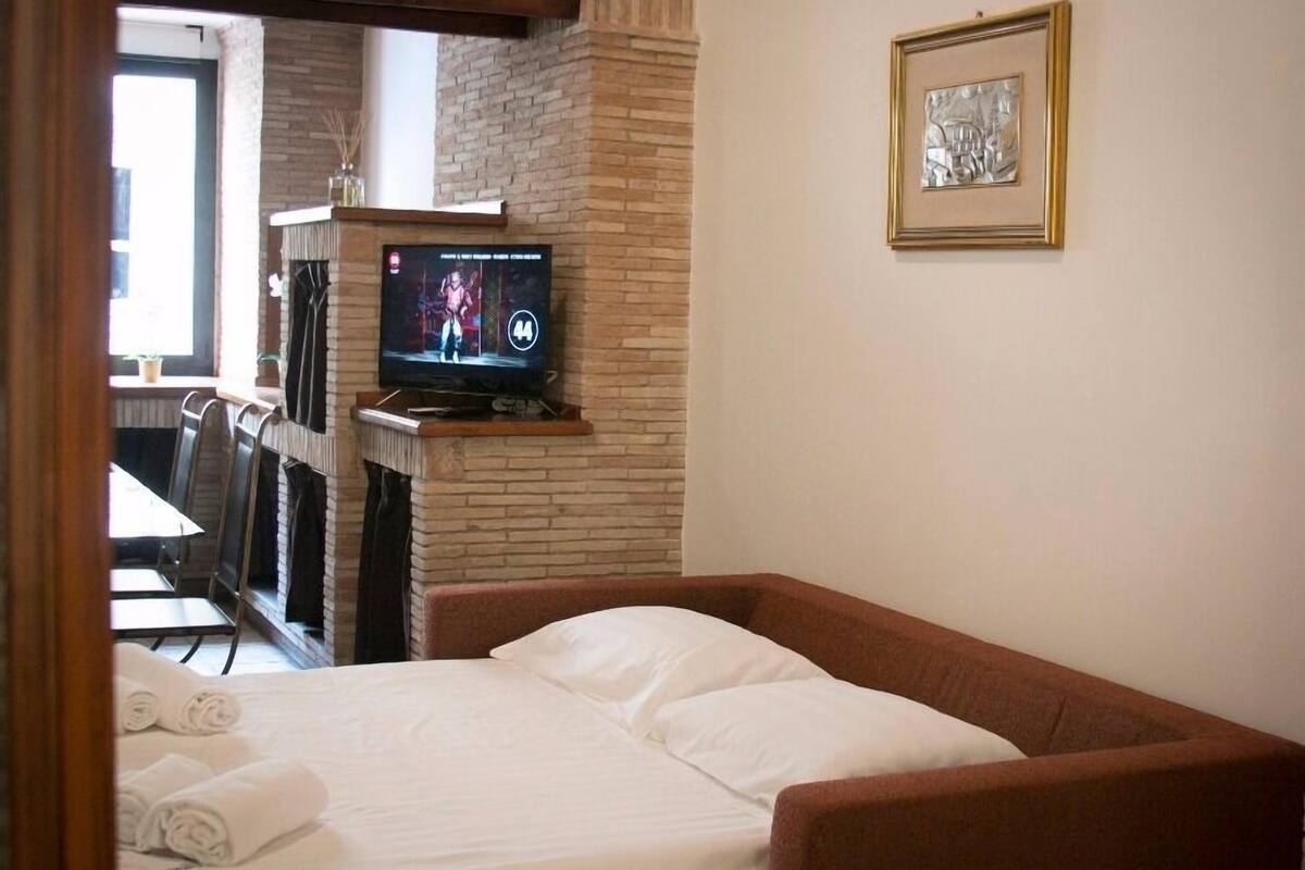 A hotel room with a bed, a television, a fireplace, and a framed picture on the wall.