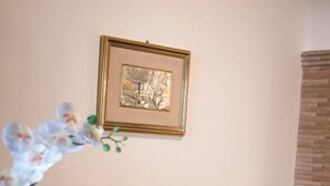 Uma sala de estar com um sofá marrom, uma mesa de centro de vidro, um quadro na parede e uma orquídea em vaso.