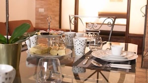Disposição para o café da manhã, com uma bandeja de doces, uma cafeteira e um conjunto de chá sobre uma mesa de vidro.
