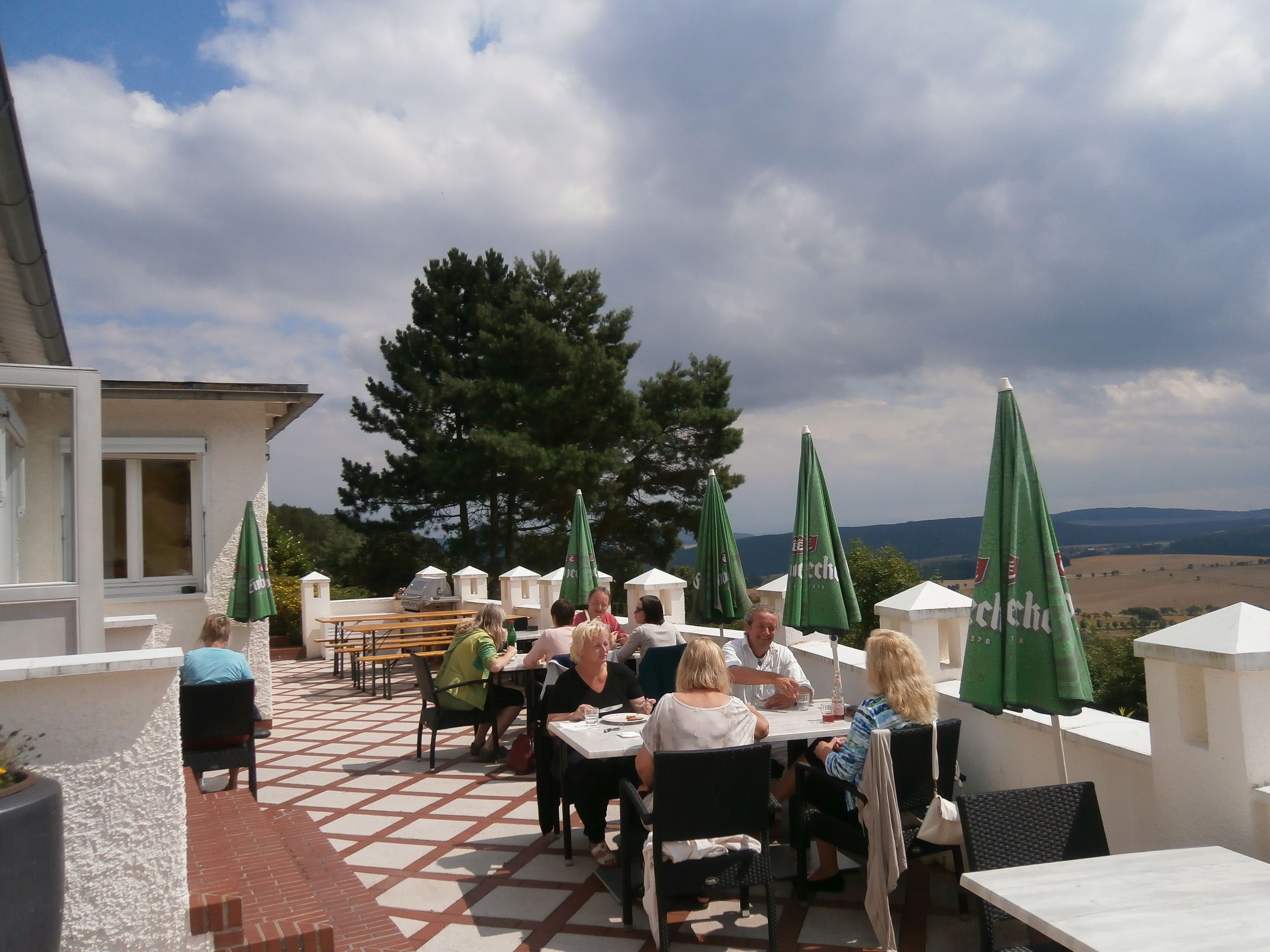 An outdoor patio with tables and chairs, green umbrellas, and a view of the landscape.