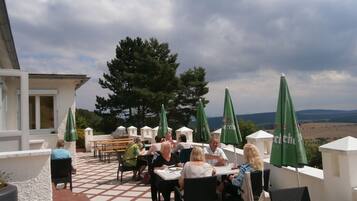 An outdoor patio with tables and chairs, green umbrellas, and a view of the landscape.