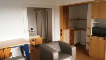 A compact living space with a kitchenette, a dining area, and a seating area with a sofa and a chair.