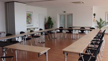 Un salón de conferencias con largas mesas y sillas, paredes blancas y una puerta con paneles de vidrio esmerilado.