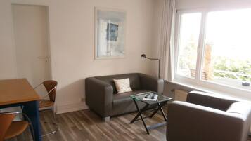 A modern living room with a sofa, armchair, glass coffee table, and a painting on the wall.