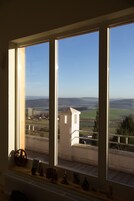 Quarto com uma grande janela com vista para uma paisagem rural, incluindo campos e uma torre pequena.