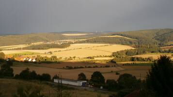 Paisagem rural com campos, um pequeno edifício e turbinas eólicas ao longe.