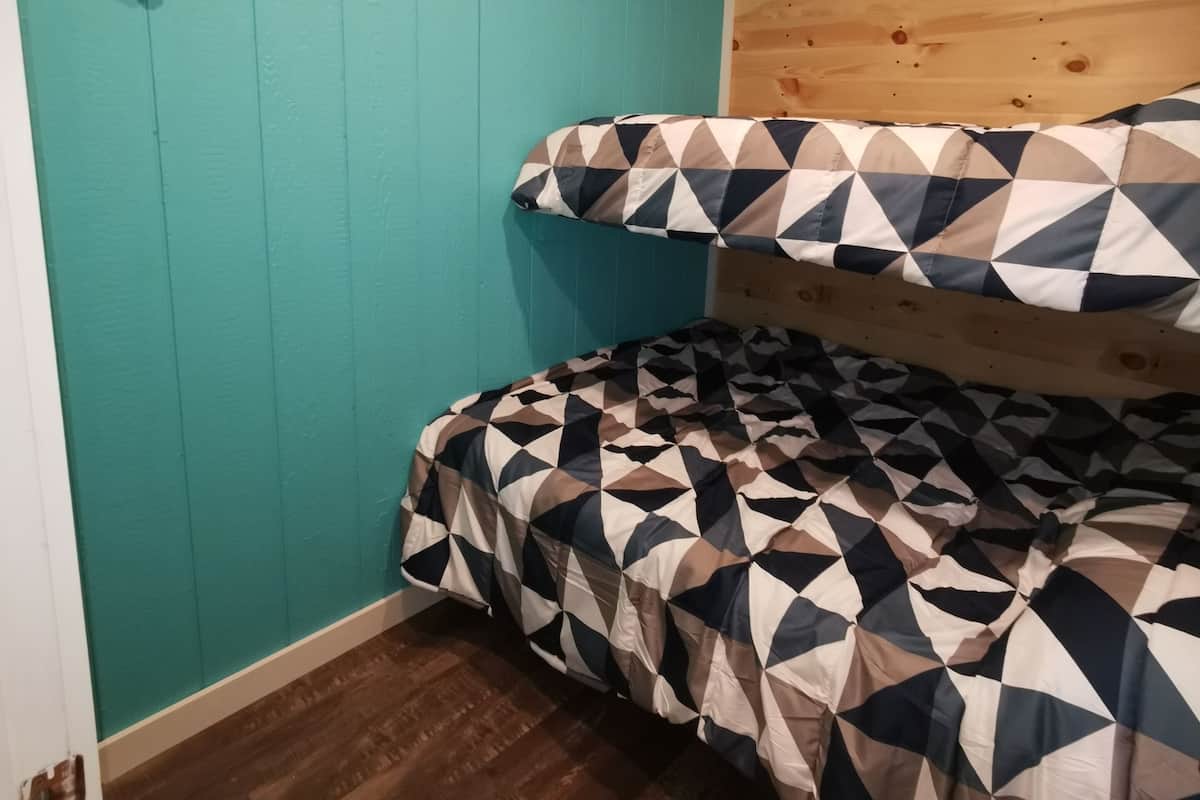 A room with teal walls, a wooden ceiling, and a bed with a geometric-patterned bedspread.