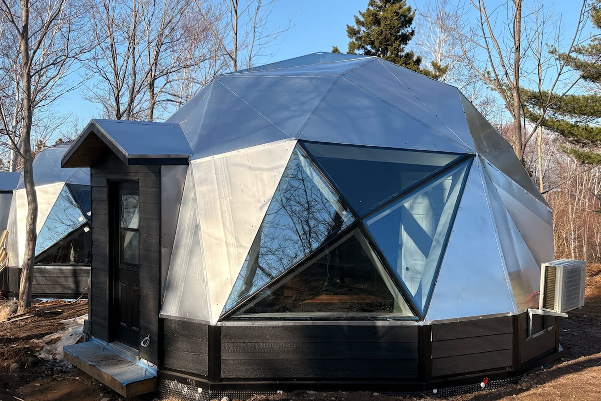 A geodesic dome structure with a wooden door and window, surrounded by trees.