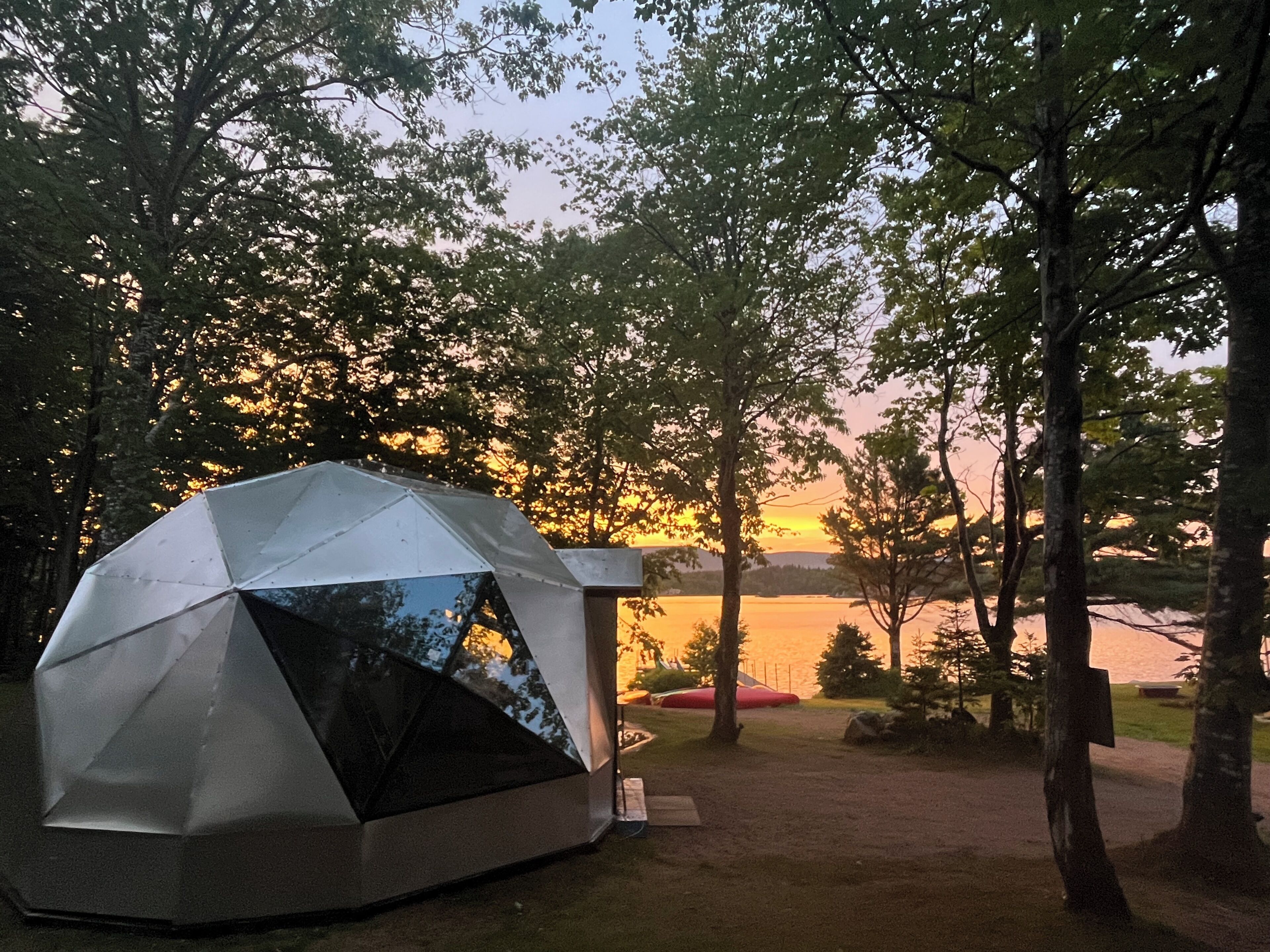 A geodesic dome structure in a natural setting with trees and a body of water in the background.