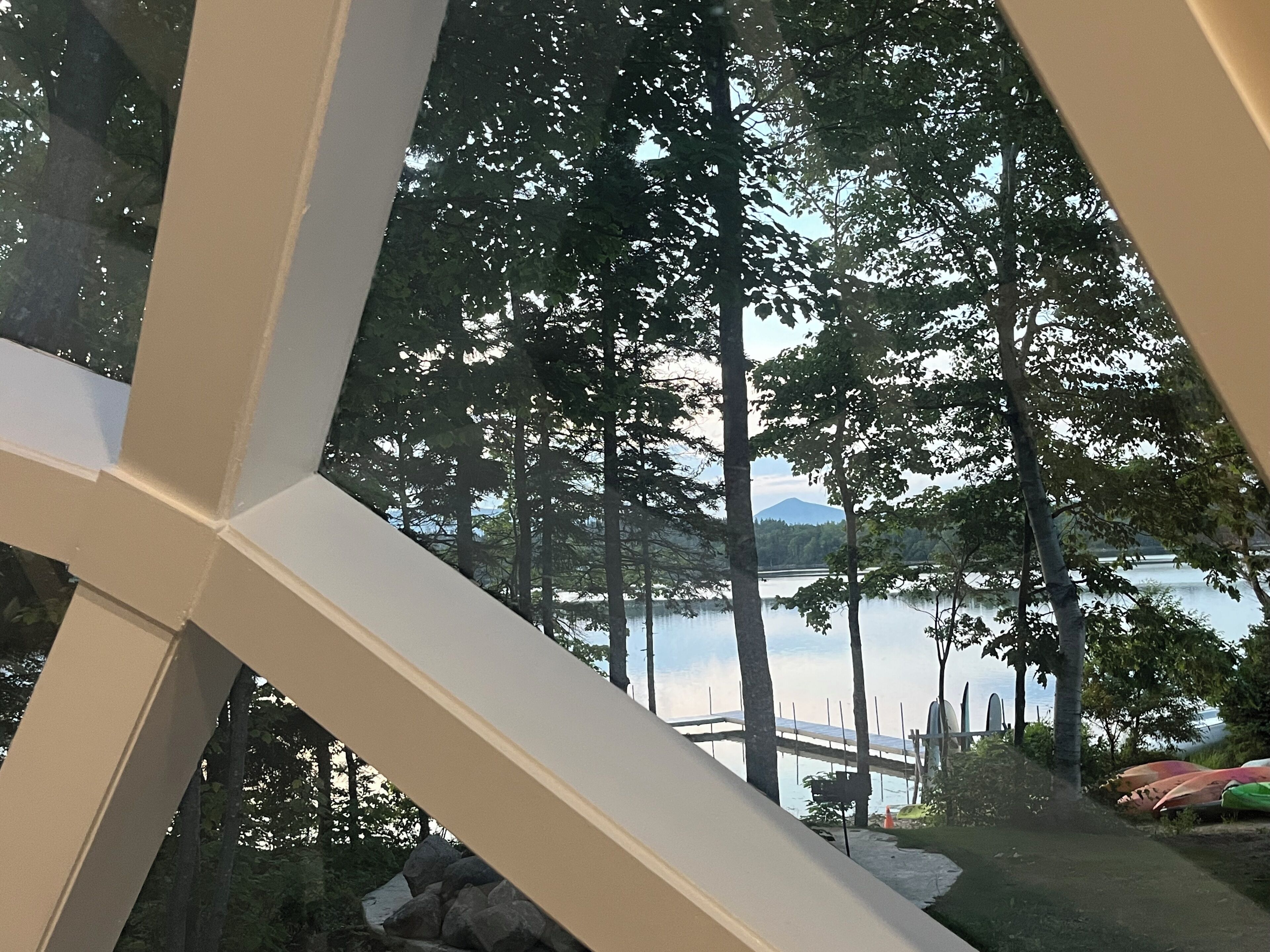 Blick durch ein Fenster mit Spiegelung von Bäumen und einem Berg in der Ferne.