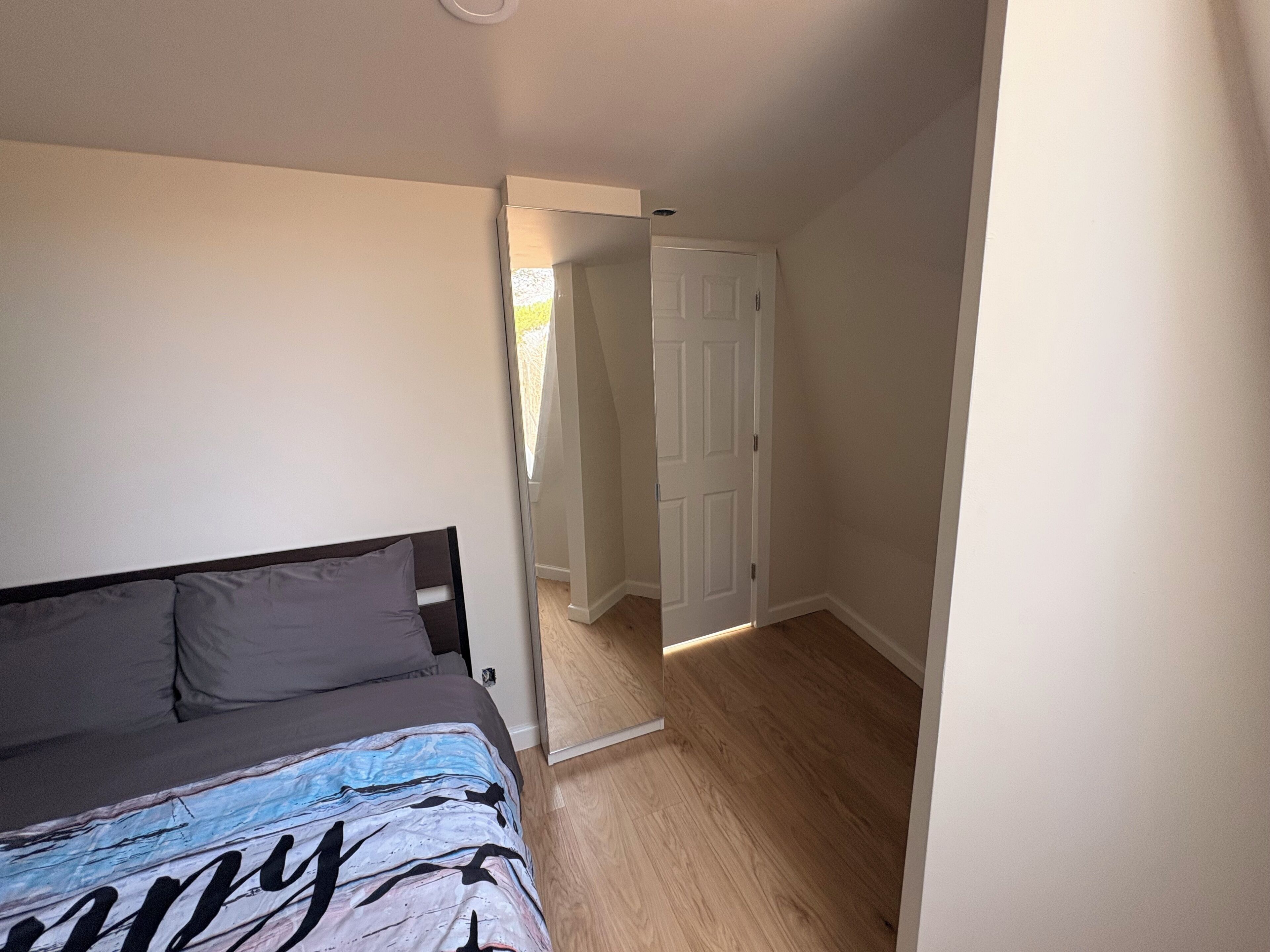 Ein Schlafzimmer mit einem Bett, einer Tür zu einem anderen Raum und einem Holzboden.