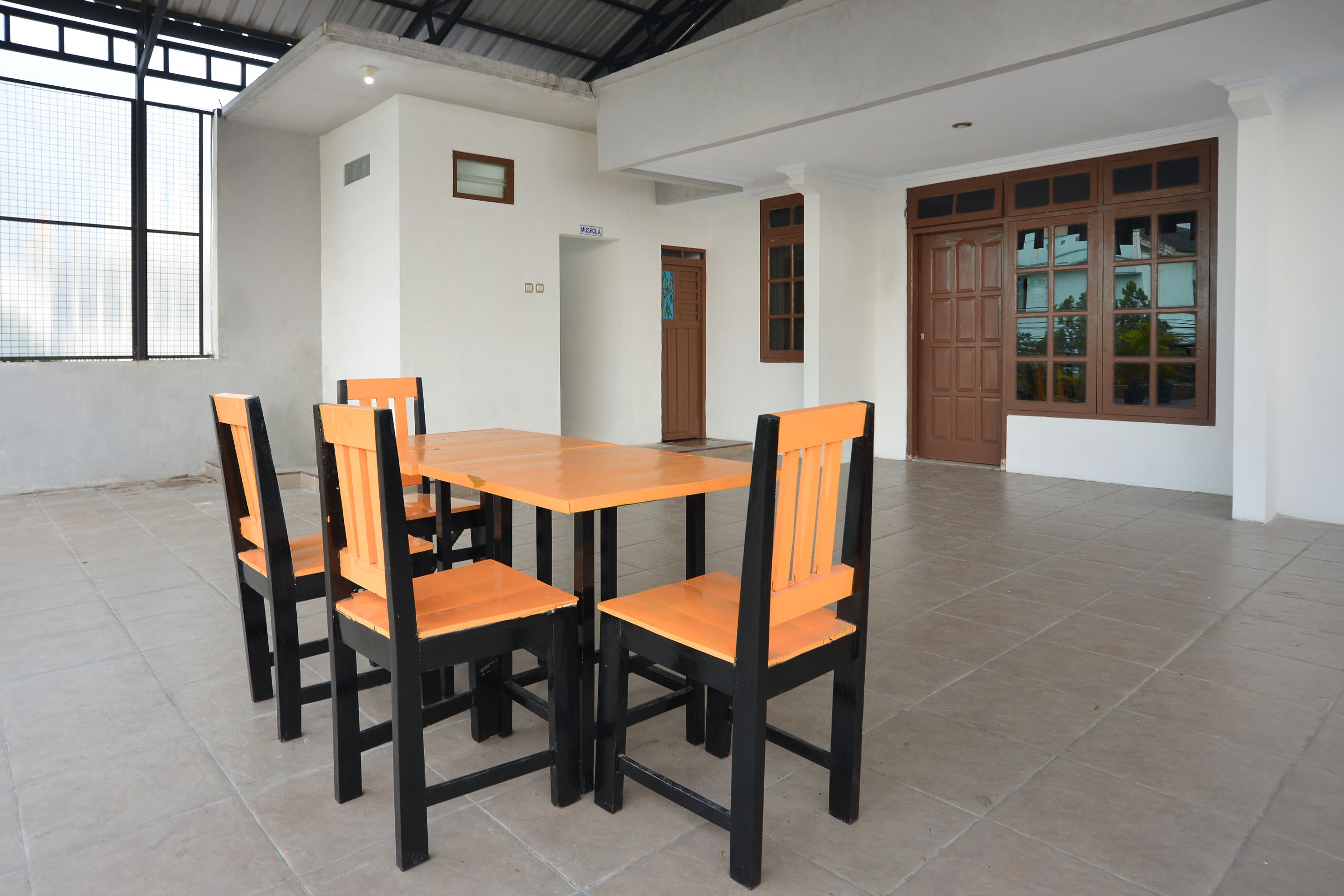 A dining area with a wooden table and chairs, a tiled floor, and large windows.