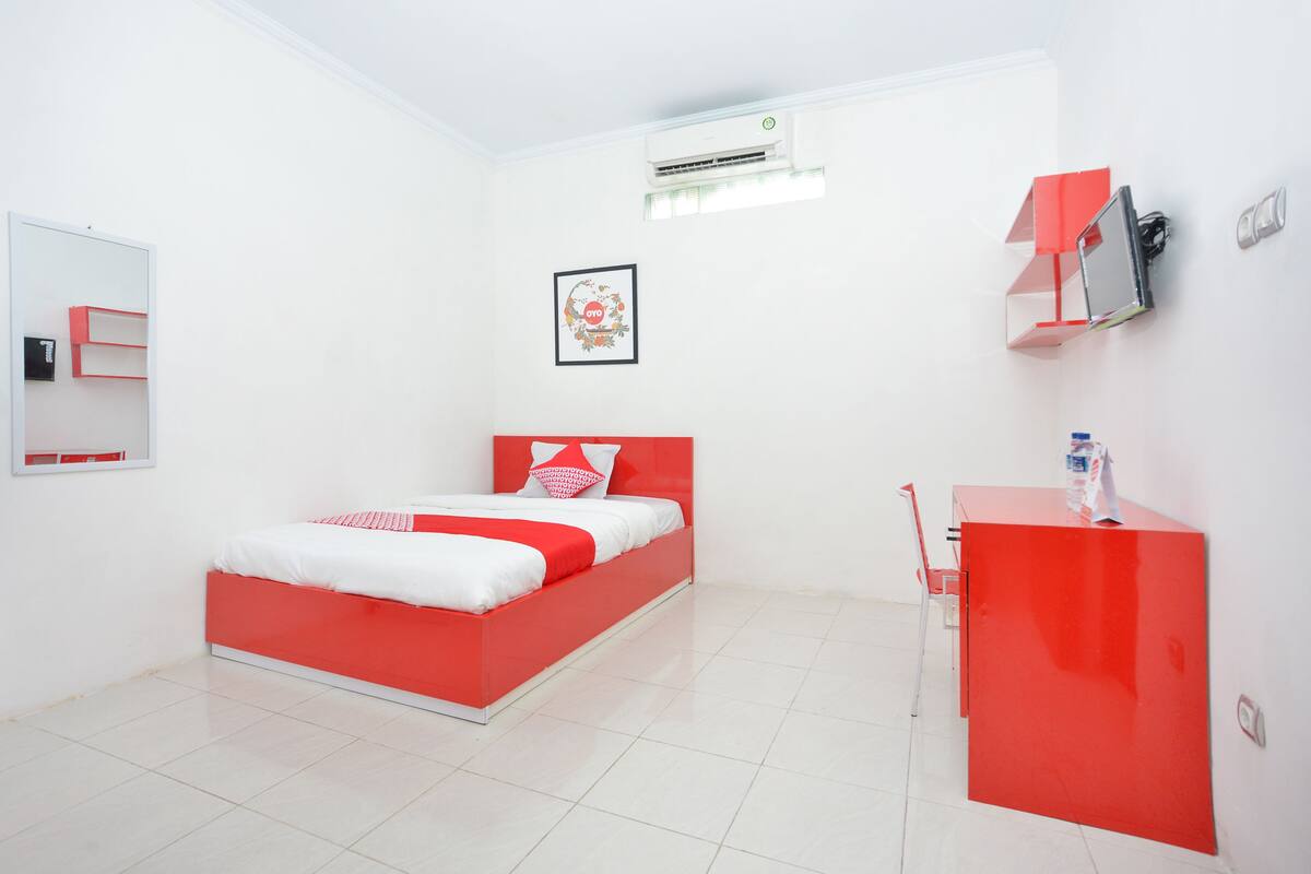 Un dormitorio moderno con una cama roja, paredes blancas y un escritorio pequeño.