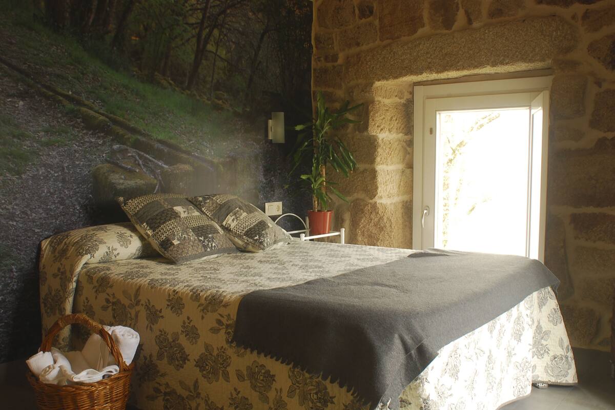 Un dormitorio con cama, una planta en maceta, una cesta y una pared de piedra.