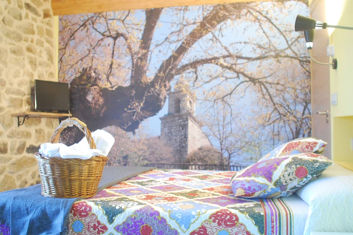 Un dormitorio con una cama, una cesta, un televisor montado en la pared y un mural de un gran árbol.