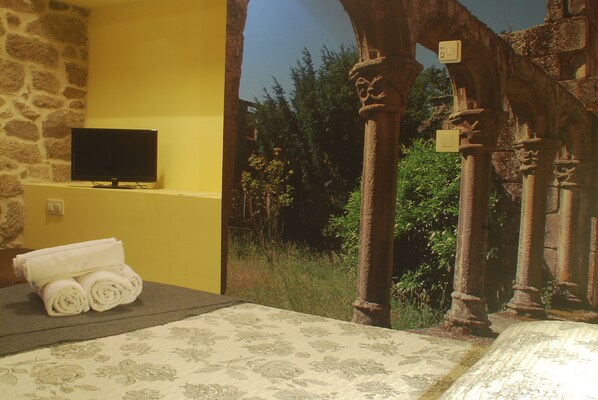 Una habitación con pared de piedra, televisor de pantalla plana, toallas enrolladas y cama con colcha estampada.