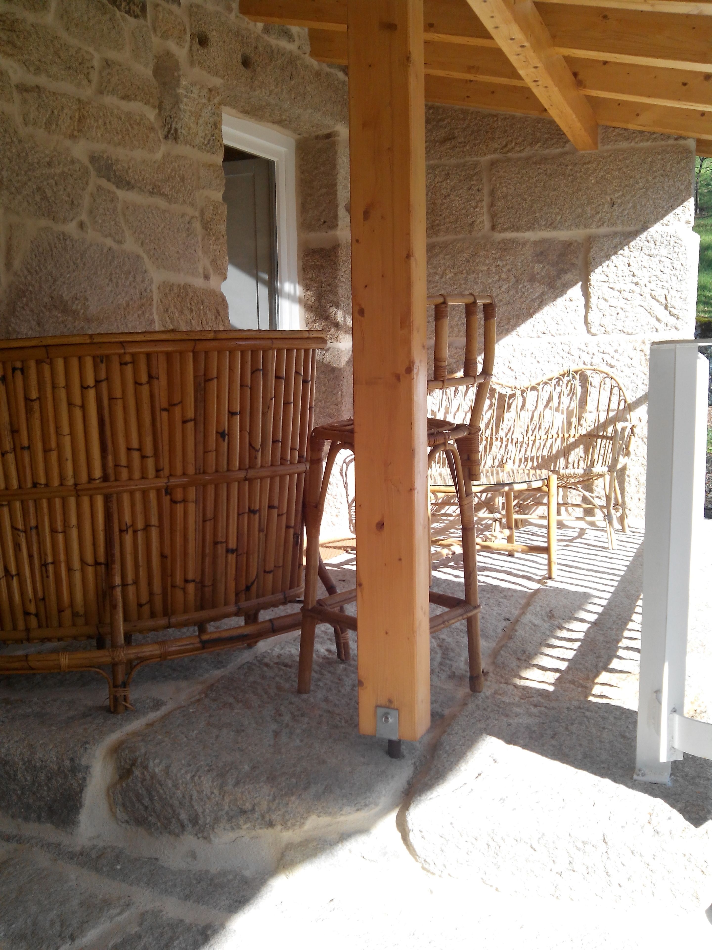 Un edificio de piedra con un porche de madera, muebles de bambú y una puerta blanca.