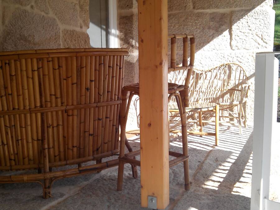 Un edificio de piedra con un porche de madera, muebles de bambú y una puerta blanca.